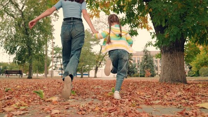 Baby, mom play together, run along path in park holding hands in autumn outdoors. Happy child runs holding his mothers hands through yellow autumn leaves. Active family walk, mother, child in park