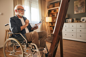 Senior man in a wheelchair painting at home