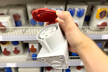 Industrial socket in a store. Selection of sockets of different colors and types for construction. Hand holding a socket close-up.