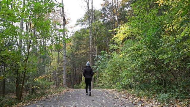 woman walking on a hiking trail in Taughannock Falls State Park (waterfall near Ithaca, finger lakes region of upstate new york) cascade, gorge, autumn, jacket, hat, fall foliage shot from behind