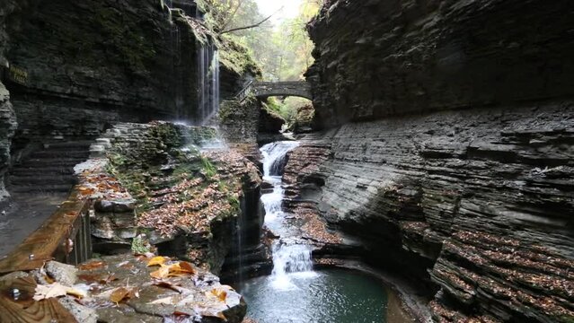water flowing at rainbow falls in watkins glen state park (waterfall, scenery, finger lakes region of new york state) beautiful autumn hiking trail with bridge and staircase inside gorge (cascade)