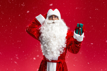Funny man wearing Santa Claus suit holding gift box looking at camera isolated on red background. Merry Christmas, winter sales concept