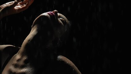 Silhouette elegant female dancing posing under rain at night. Seductive woman, gymnast dancer wearing black swimsuit, raindrops splashes, water drops roll down sexy body in shower, black background
