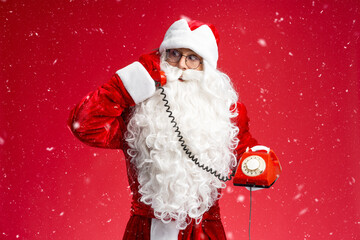 Santa Claus holding retro telephone answering call, listening wish isolated on red background. Winter holidays concept 