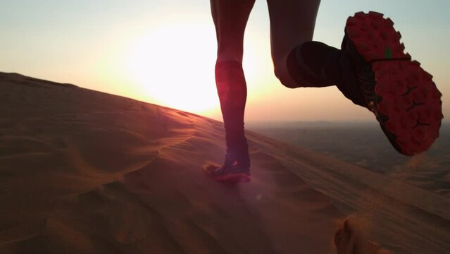 Man in running shoes kicking up sand as he runs in the desert at sunrise