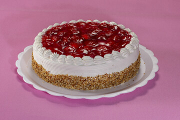 Delicious pie with peanuts and strawberry on a white plate on a pink textured background.