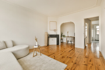 a living room with white walls and wood flooring in the center of the room is an arched doorway...