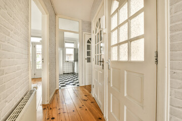 a hallway with wood flooring and white brick wall behind the door to the left is a black and white checkereded tile