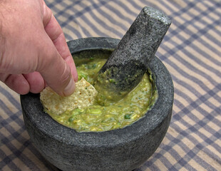 hand dipping tortilla chip into guacamole inside molcajete (traditional mexican mortar and pestle...