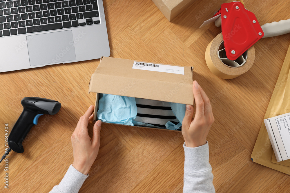 Sticker Woman packing clothes at wooden table, top view. Online store