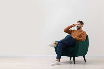Handsome man sitting in armchair near white wall indoors, space for text - Powered by Adobe