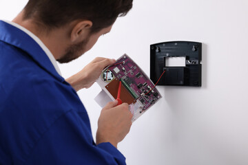 Technician installing home security alarm system on white wall indoors