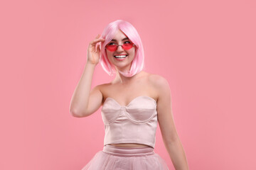 Pink look. Beautiful girl in wig and clothes wearing bright sunglasses on color background