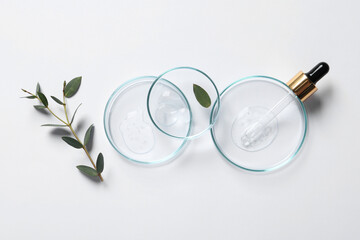 Petri dishes with samples of cosmetic oil, pipette and green leaves on white background, flat lay
