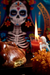 Bread of the dead with marigold flowers decorated with lit candles, in the background a catrina skull dressed in gala clothes