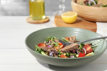 Delicious salad with beef tongue, vegetables and fork served on white wooden table