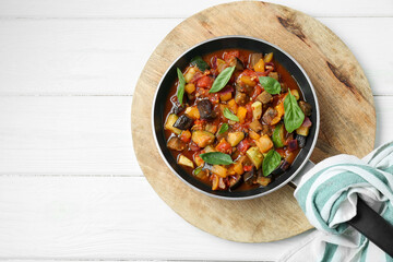 Frying pan with tasty ratatouille on white wooden table, top view. Space for text