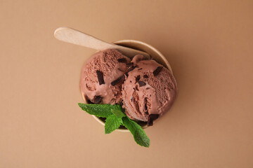 Paper cup with tasty chocolate ice cream, sticks and mint leaves on light brown background, top view