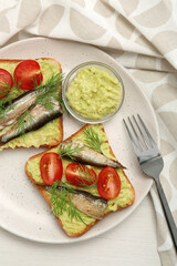 Delicious sandwiches with sprats, tomatoes, dill and avocado puree served on white wooden table, top view