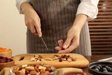Making granola. Woman cutting nuts at table in kitchen, closeup