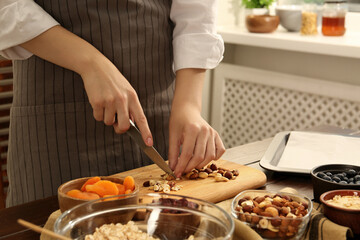 Obraz na płótnie Canvas Making granola. Woman cutting nuts at table in kitchen, closeup