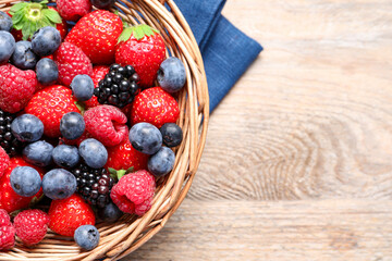 Many different fresh ripe berries in wicker basket on wooden table, top view. Space for text