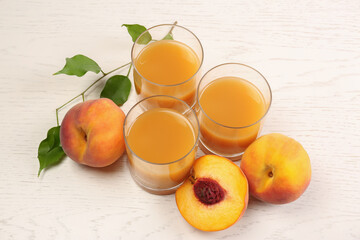 Glasses of delicious peach juice, fresh fruits and leaves on white wooden table, above view