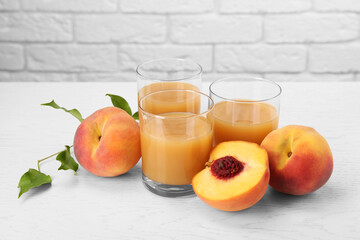 Glasses of delicious peach juice, fresh fruits and leaves on white wooden table