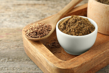 Caraway (Persian cumin) powder and dry seeds on wooden table, closeup