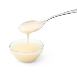 Condensed milk flowing down from spoon into bowl isolated on white
