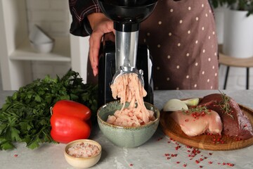 Woman making chicken mince with electric meat grinder at grey marble table indoors, closeup