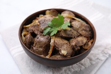 Tasty fried chicken liver with onion and parsley in bowl on white table, closeup
