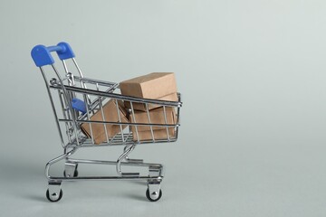 Small metal shopping cart with cardboard boxes on light background, space for text