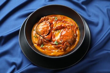 Delicious boiled crabs with sauce in bowl on blue tablecloth
