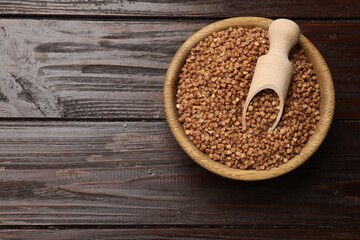 Bowl and scoop with dry buckwheat on wooden table, top view. Space for text