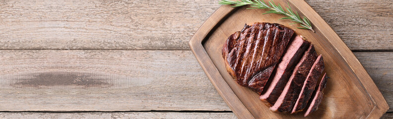 Delicious fried beef meat with rosemary on wooden table, top view. Banner design with space for text