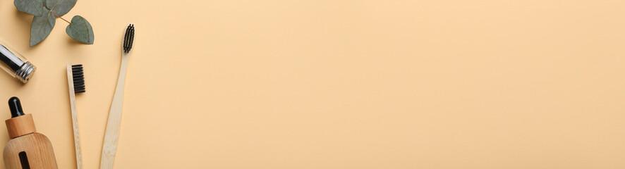 Bamboo toothbrushes, cosmetic products and leaves on beige background, flat lay. Banner design with space for text