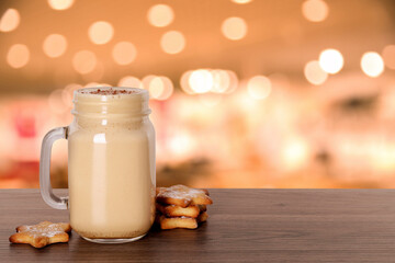 Mason jar with delicious eggnog and cookies on wooden table in bar, space for text