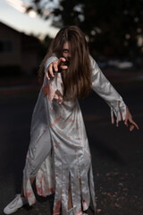 One Teen Girl in Bloody Zombie Costume, Reaching Toward Camera, on Halloween Night, vertical © greeeniiii17