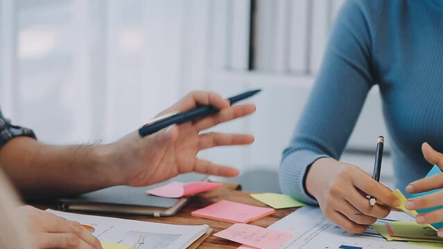 Two creative business people meeting and planning use post it notes sticky note on desk to share idea, Analysis data chart and graph with teamwork strategy brainstorming in office.