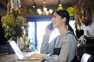 花屋でスマートフォンとパソコンを使って働く日本人女性