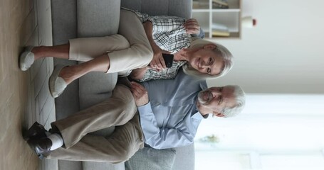 Positive elderly retired couple discussing online medical service, healthcare application on mobile phone, using Internet technology for wireless communication, resting on home couch with smartphone - Powered by Adobe