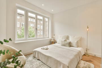 a bedroom with a bed, chair and lamp in front of the window that looks out onto an apartment block