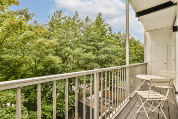 a balcony with white furniture and trees in the background on a bright sunny day, as seen from an apartment balcony