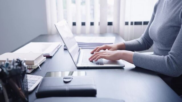 Confident Asian businesswoman working on her computer laptop, using analytical thinking to focus on her tasks diligently. She demonstrates a strong work ethic and determination