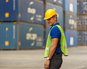 Caucasian man wearing yellow safety helmet Wear a reflective safety suit, hold a tablet, and stand smiling against a container. In the container storage yard