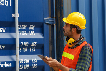 Caucasian man wearing yellow safety helmet Wear reflective safety clothing. Carrying a tablet to inspect the product In the container storage yard