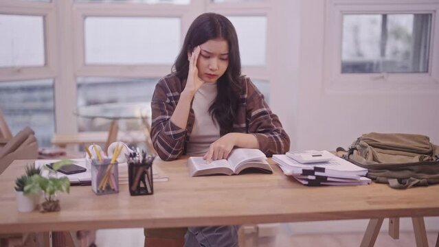 Asian schoolgirl in her study attire is immersed in her books, preparing diligently for an upcoming exam. Her commitment is so unwavering that she finds herself dozing off on the desk i dorm room.