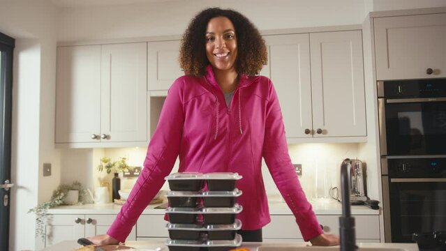 Portrait of smiling woman in kitchen wearing fitness clothing making batch of healthy meals in advance for fridge - shot in slow motion