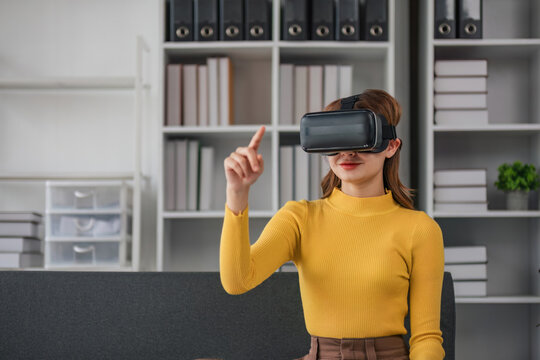 Charming Asian woman plays games in virtual reality through VR glasses on the sofa with a fun and entertaining time in your living room at home.